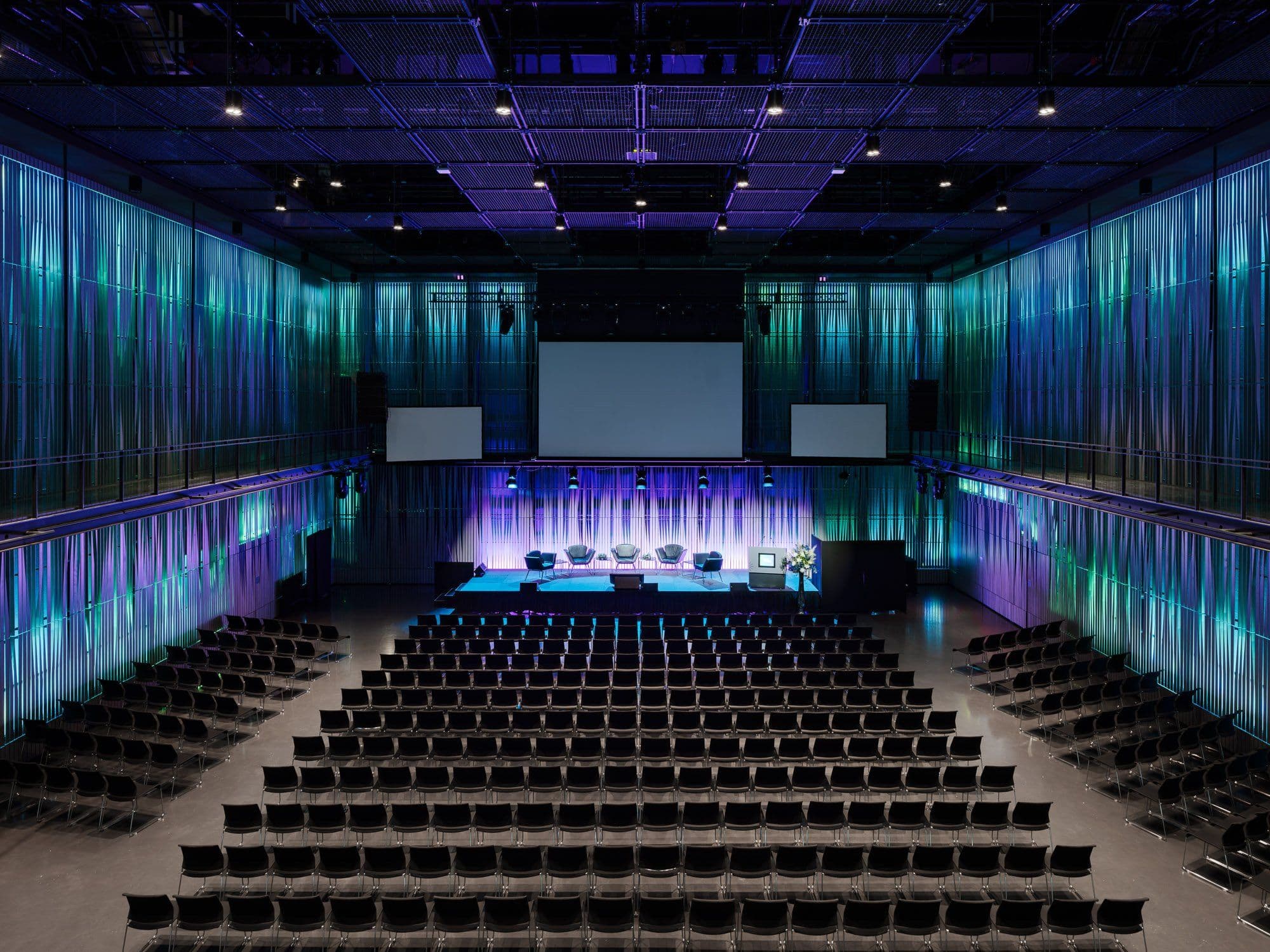 a large auditorium filled with rows of chairs and purple lights .