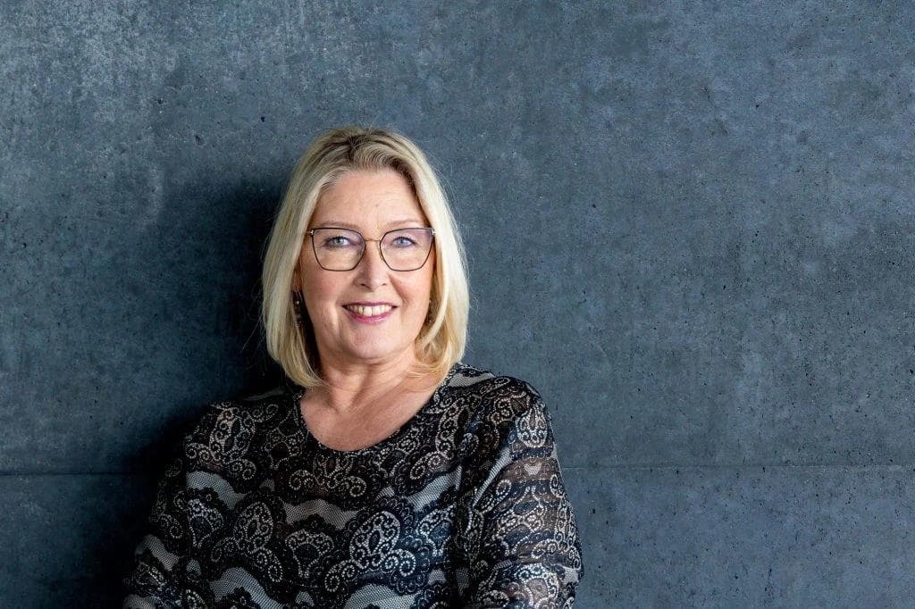 a woman wearing glasses and a dress is standing in front of a gray wall .